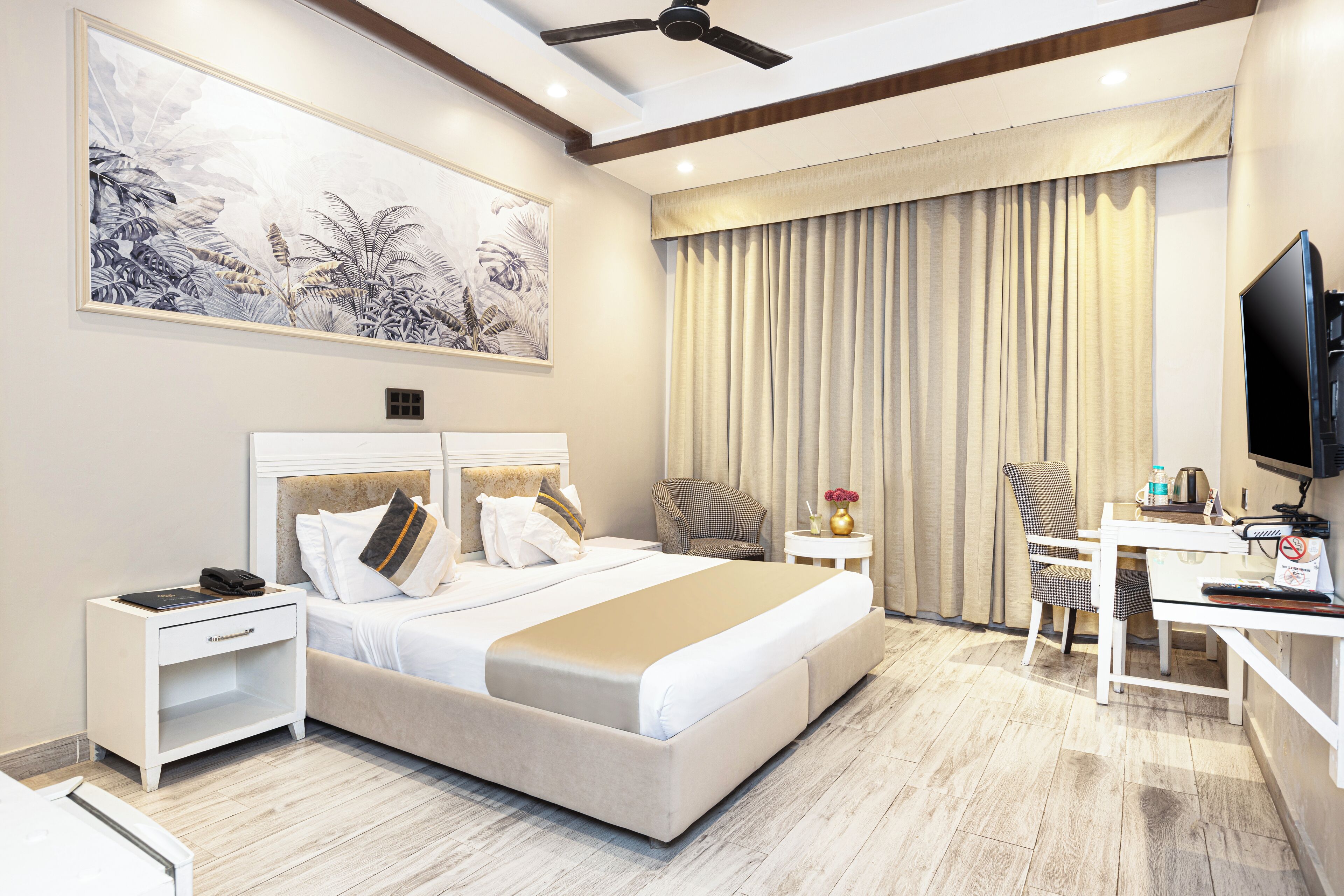 A modern hotel room with a large bed, a desk, a chair, a television, and a ceiling fan.