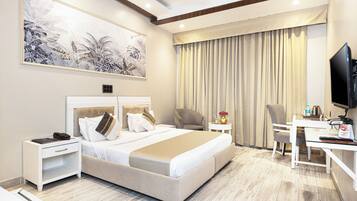 A modern hotel room with a large bed, a desk, a chair, a television, and a ceiling fan.