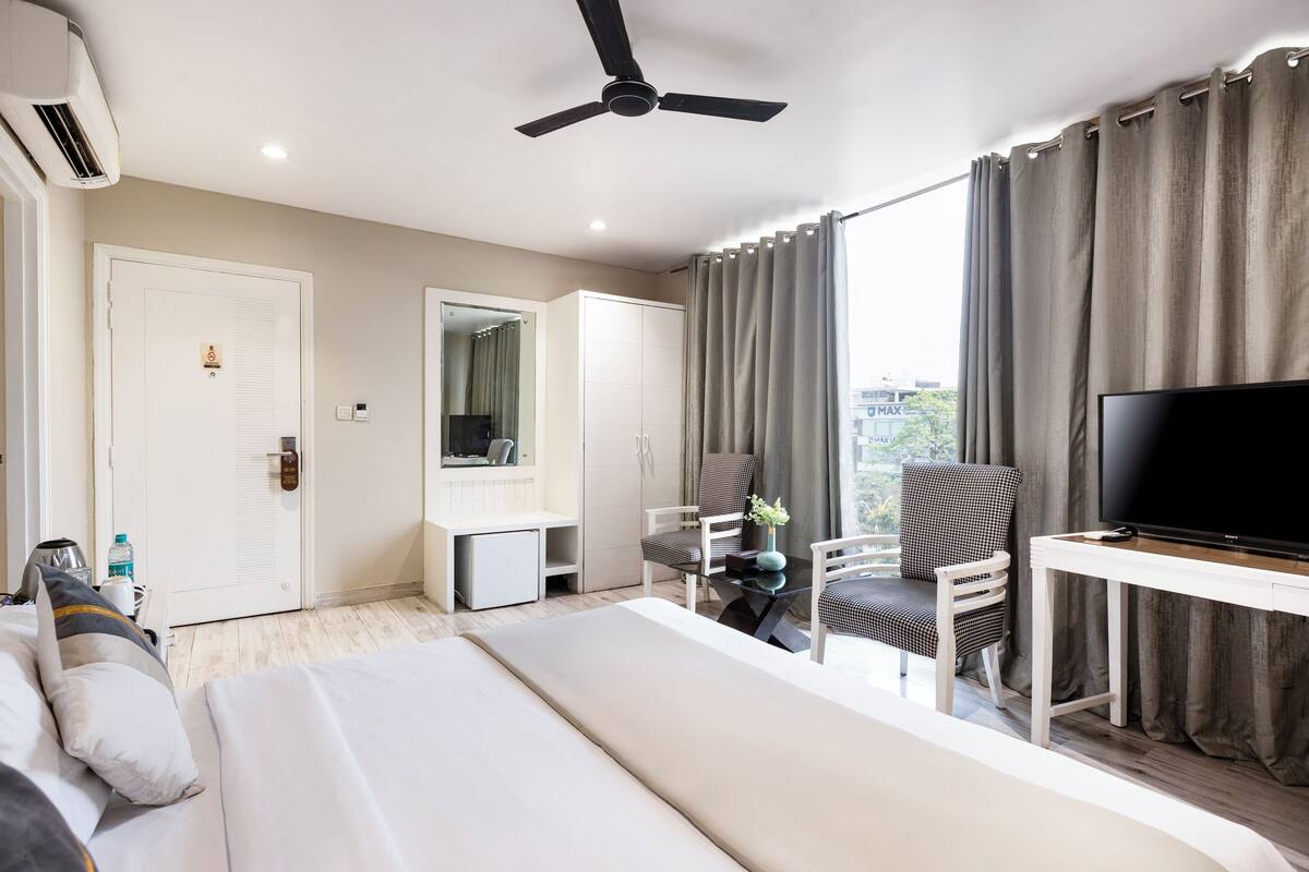 A modern hotel room with a bed, a TV, a desk, and a chair.