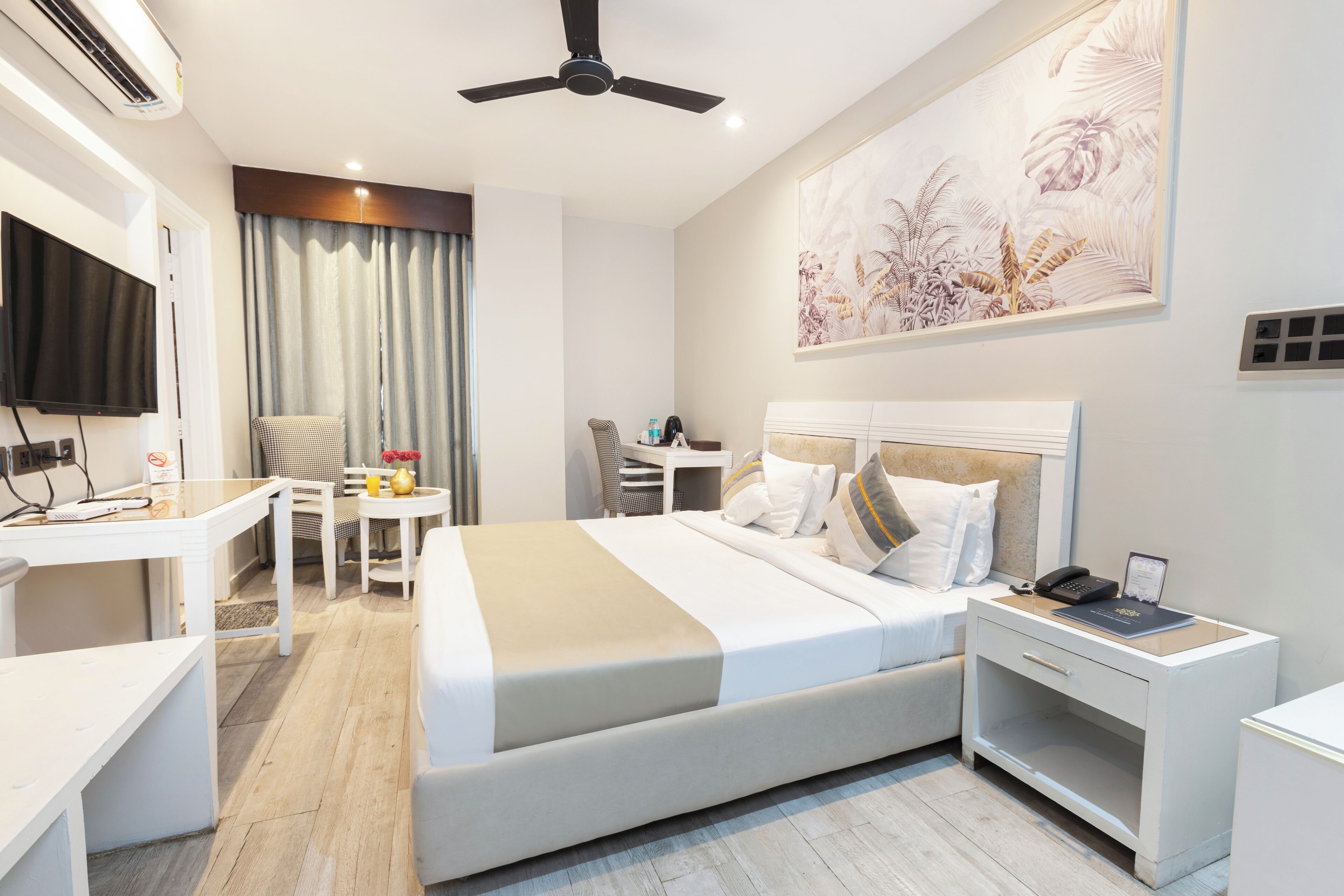 A modern hotel room with a large bed, bedside table, and a desk with a chair.