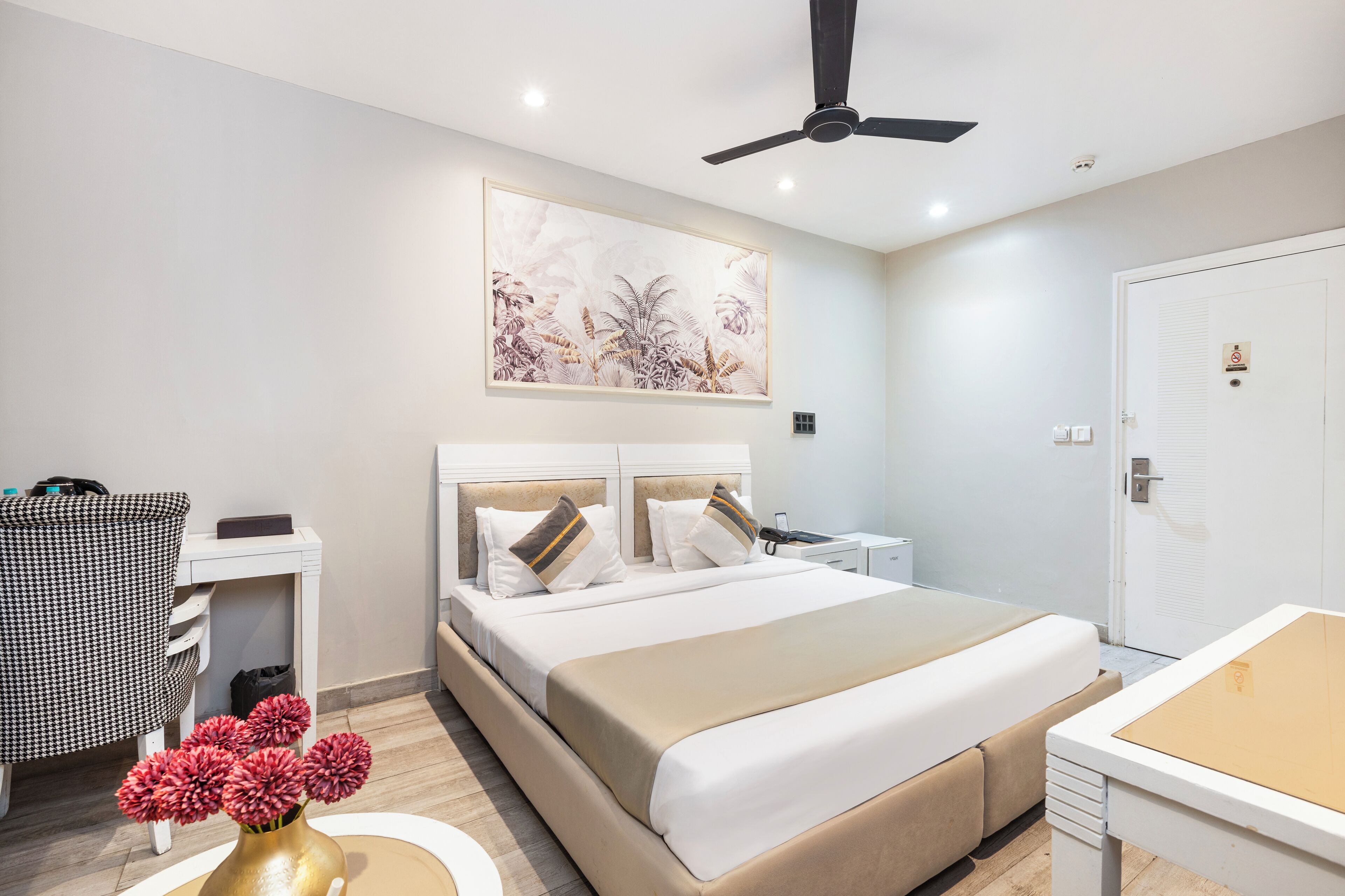 A modern hotel room with a large bed, a desk, a chair, and a ceiling fan.