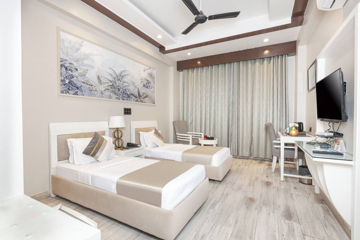 A hotel room with two beds, a desk, a chair, a television, and a large window with curtains.