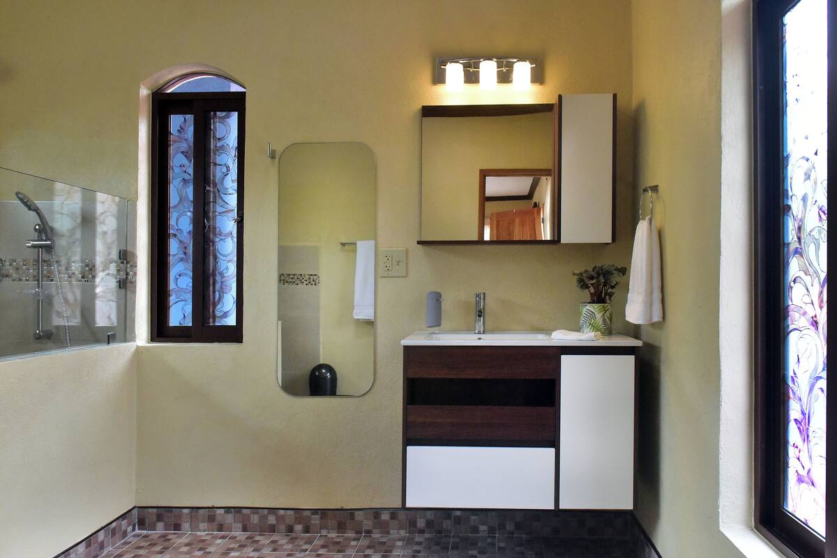 Une salle de bain avec une douche à parois de verre, un meuble-lavabo avec un miroir et une fenêtre donnant sur un beau paysage.