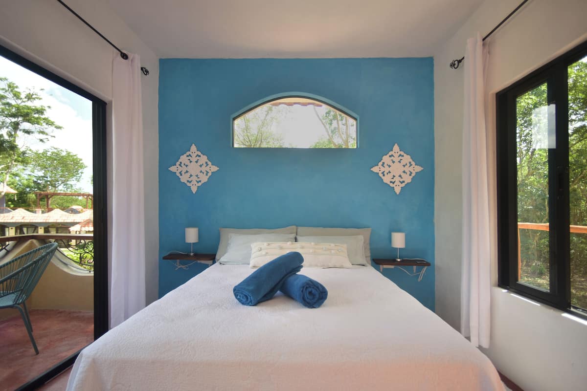 Une chambre à coucher avec un grand lit, deux tables de chevet, une fenêtre et une vue sur l’extérieur.