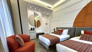 Una camera d'albergo moderna con due letti, una sedia rossa e una piccola scrivania con specchio e lampada.