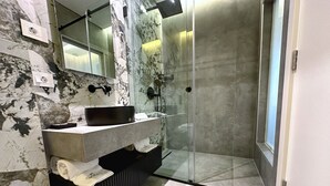Un bagno moderno con zoccolo in marmo, lavabo nero e cabina doccia in vetro.