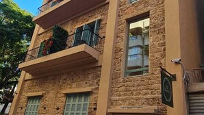 Un edificio a più piani con facciata in pietra, balconi con piante e una scalinata che conduce all'ingresso.