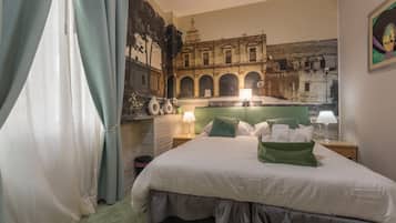 Een hotelkamer met een groot bed, een nachtkastje met een lamp, een spiegel aan de muur en een muurschildering van een oud gebouw.