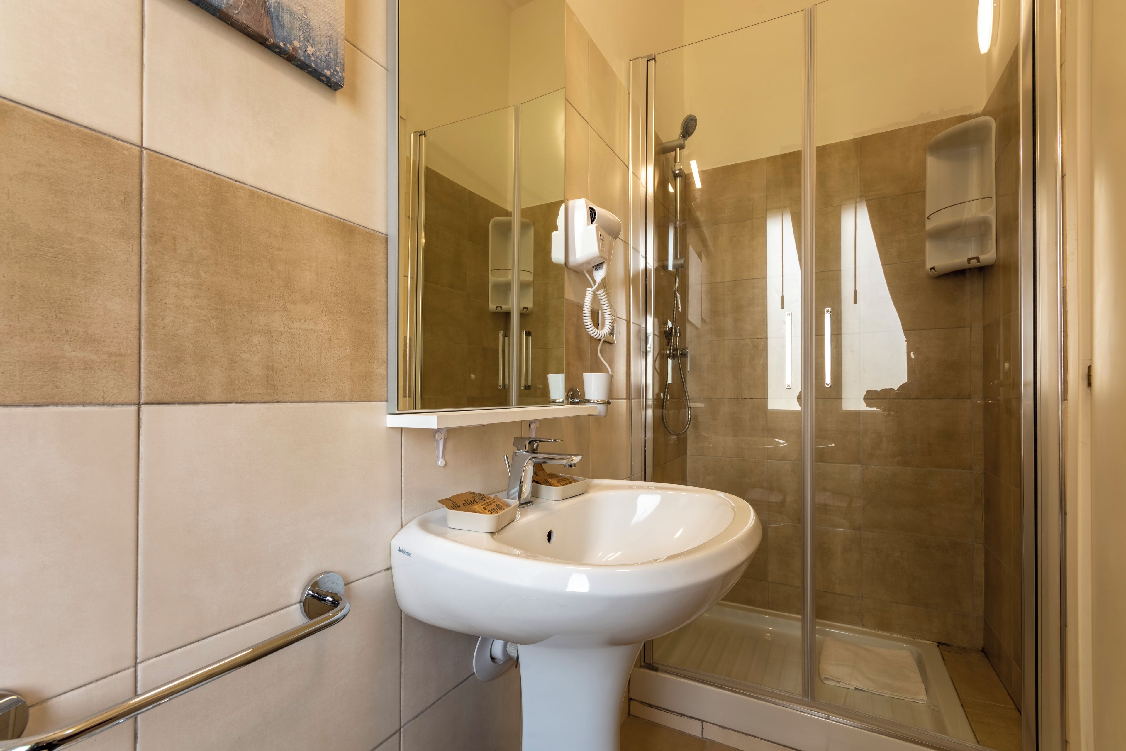 Un bagno moderno con box doccia in vetro, un lavandino bianco e un asciugacapelli portatile fissato alla parete.