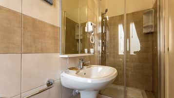 Un bagno moderno con box doccia in vetro, un lavandino bianco e un asciugacapelli portatile fissato alla parete.
