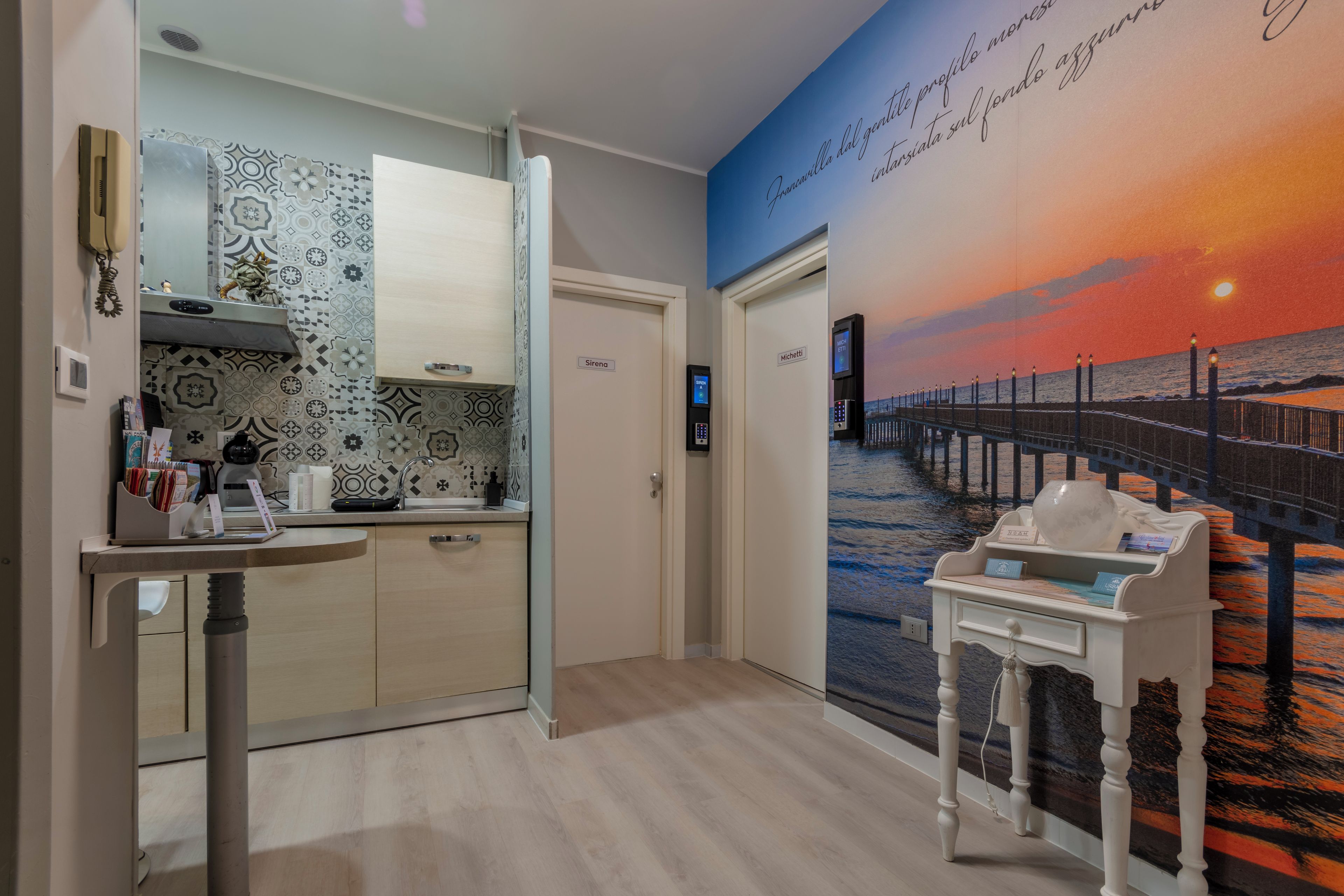 A modern kitchen with patterned backsplash, a dining area with a view of a sunset over the ocean, and a small table with a vase.