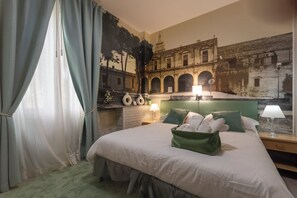 Une chambre d’hôtel avec un lit, une tête de lit, une table de chevet, une lampe, un oreiller vert et une fresque murale.