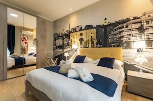 Quarto de hotel com uma cama grande, um espelho, um mural com vista para a cidade e uma mesa de cabeceira com abajur.
