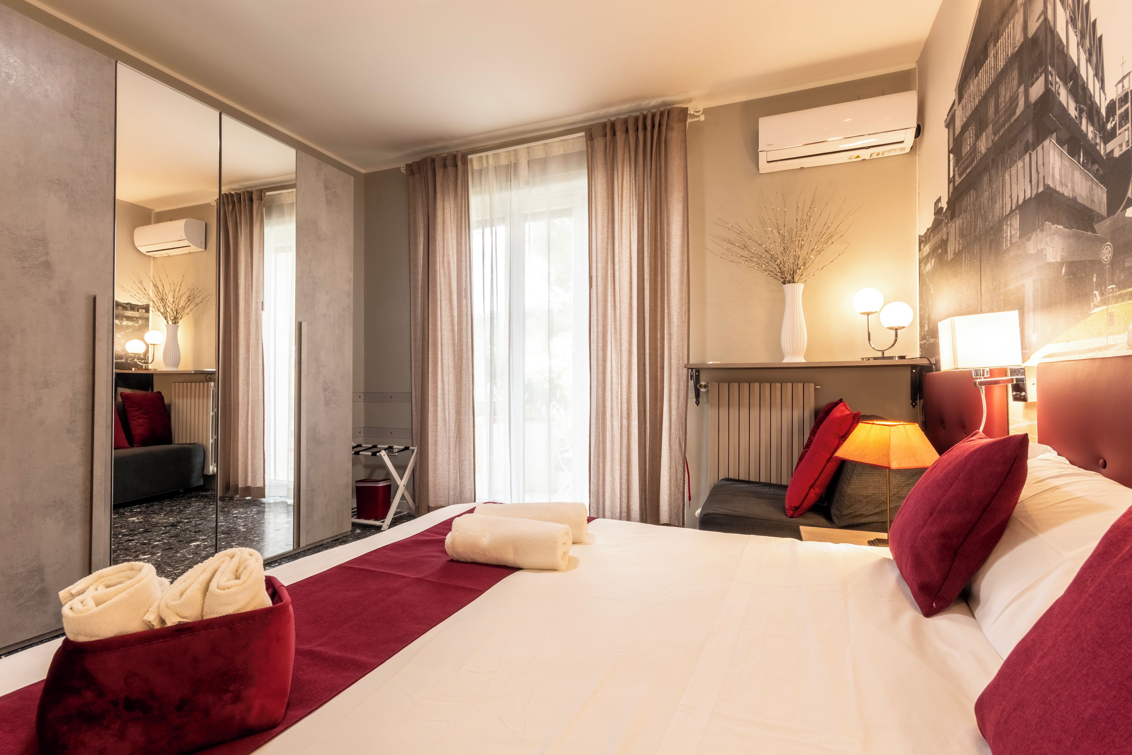Camera d'albergo con un letto grande, uno specchio, un termosifone e vista su un edificio dalla finestra.