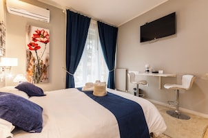 Quarto de hotel com cama, escrivaninha, cadeira, televisão e janela com cortinas.