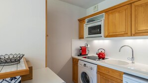 A compact kitchen with wooden cabinets, a built-in oven, a washing machine, and a sink.