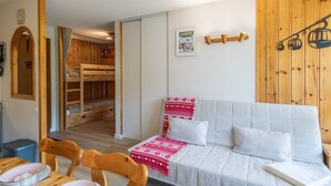 A cozy room with a bunk bed, a sofa with a patterned throw, and a wooden wall with a ski lift illustration.