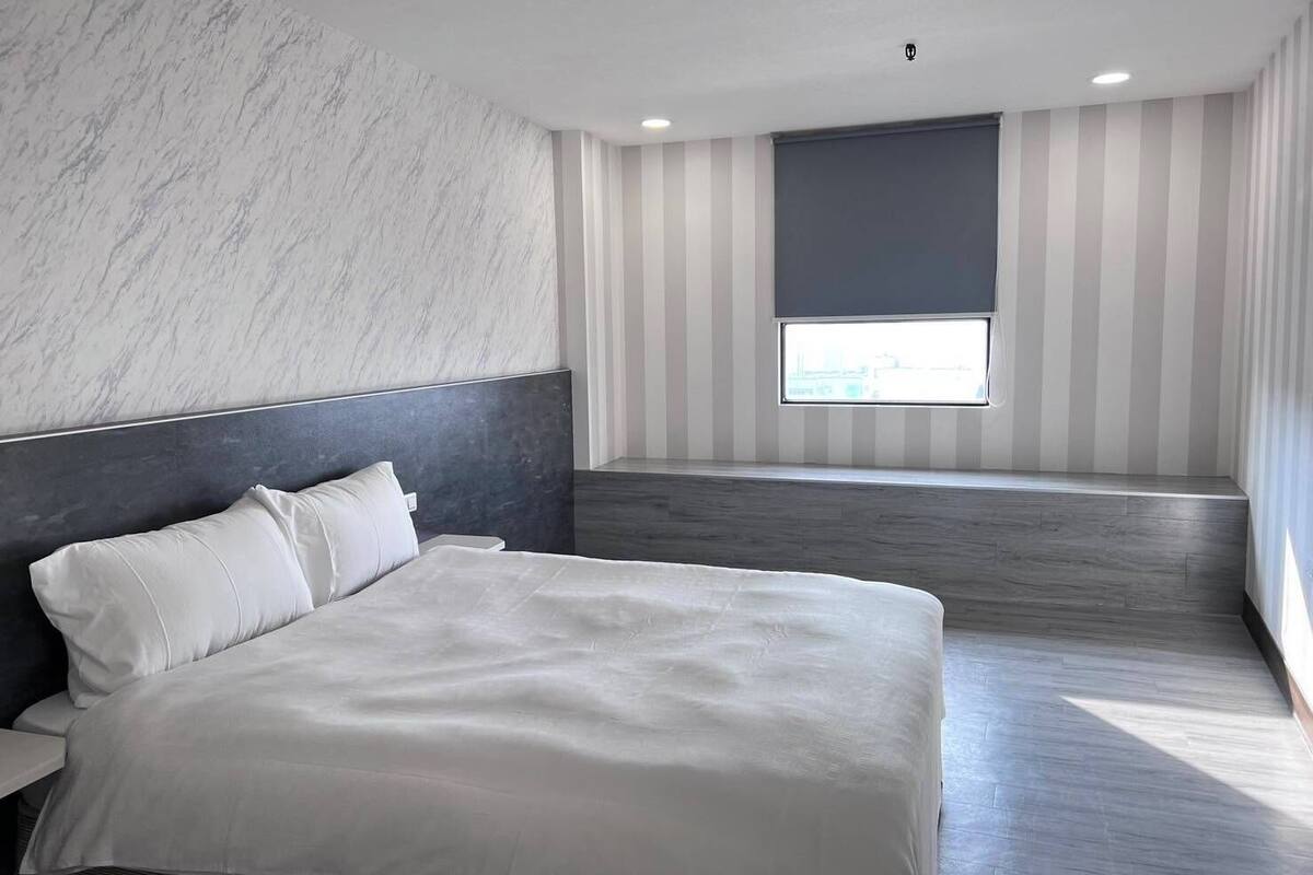 Un dormitorio moderno con una cama grande, cabecera, ventana con persianas y pared a rayas.