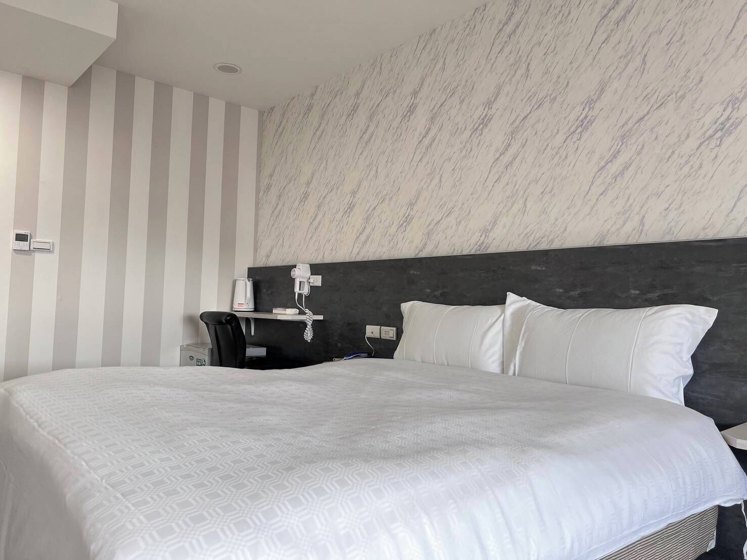 A modern hotel room with a large bed, a desk with a telephone, and a marble-patterned wall.