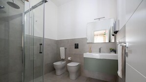A modern bathroom with a glass shower enclosure, two toilets, a sink, and a mirror.