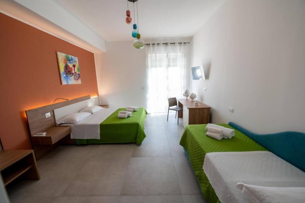 Een hotelkamer met twee eenpersoonsbedden, een bureau, een stoel en een kleurrijk abstract schilderij aan de muur.
