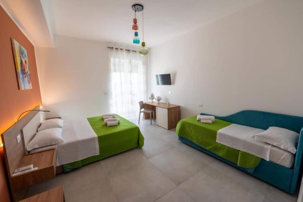 Hotelkamer met twee éénpersoonsbedden, een bureau, een stoel, een televisie en een raam met gordijnen.