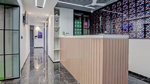 Uma área de recepção de hotel moderna, com piso de mármore, balcão de madeira e parede decorativa com padrões geométricos.