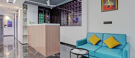 Eine moderne Lobby mit einer Rezeption, einem blauen Sofa mit gelben Kissen und einem gerahmten Kunstwerk an der Wand.