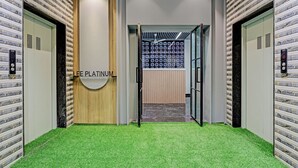 Área de elevador com piso de grama artificial, painel de madeira e uma placa com a inscrição 'LEE PLATINUM'.