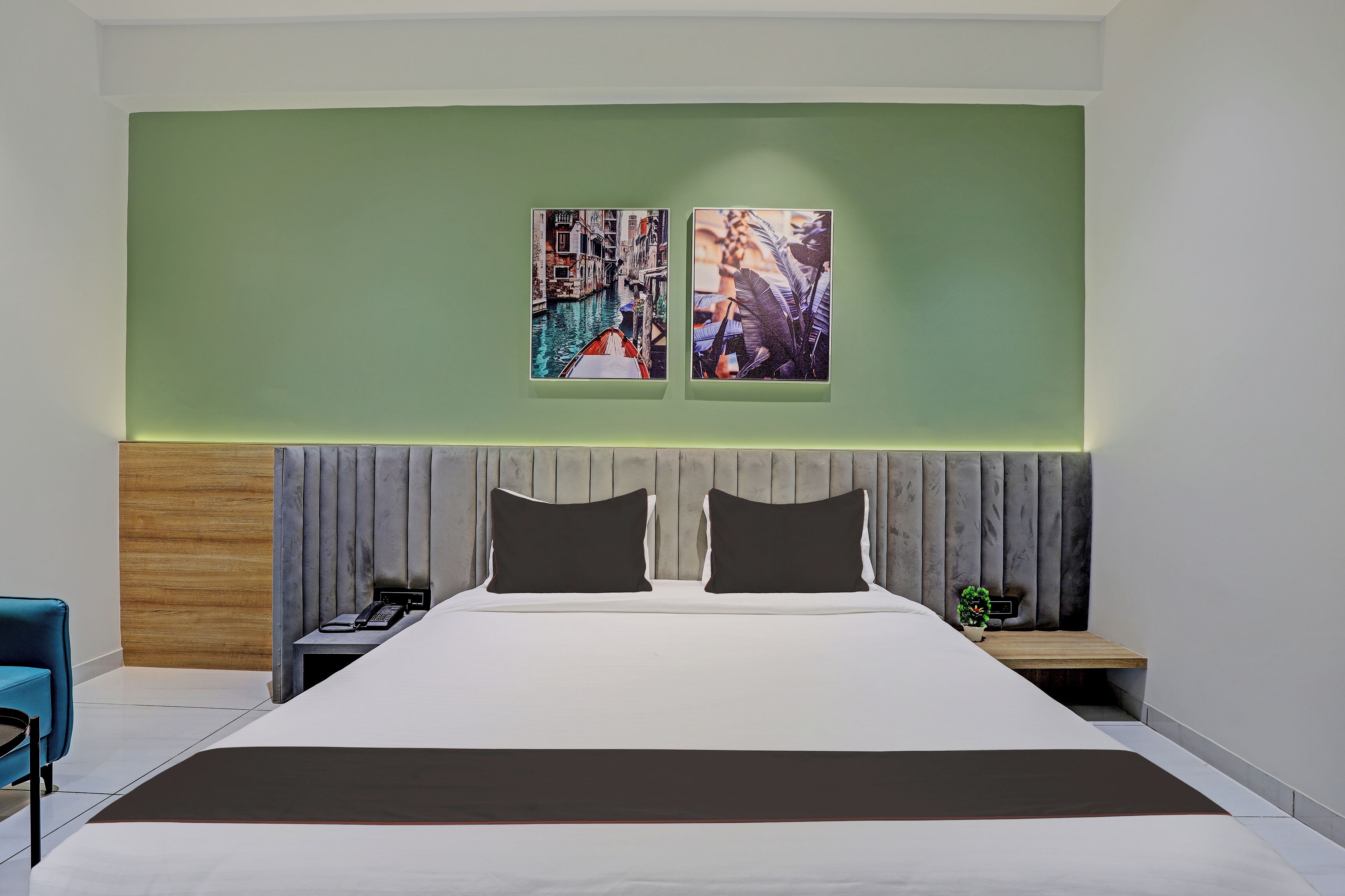 Quarto de hotel moderno com uma cama grande, cabeceira de madeira, mesa de cabeceira e duas pinturas penduradas na parede.