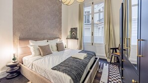Een moderne slaapkamer met een groot bed, nachtkastje, dressoir en uitzicht op de stad door een raam.
