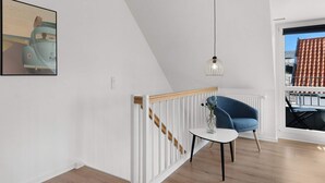 A modern living room with a white railing, a blue chair, a small table, and a hanging light fixture. - 5 Star Holiday Home in Lokken (Lokken)