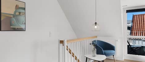 A modern interior with a staircase, a blue chair, a table, and a pendant light.