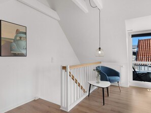 A modern interior with a staircase, a blue chair, a table, and a pendant light.