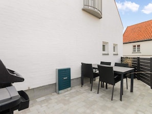 A patio with a table and chairs, a green utility box, and a white building with a red-tiled roof.