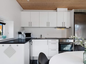 Una cocina moderna con armarios blancos, un refrigerador de acero inoxidable, una cafetera y un lavamanos.