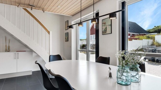 A modern kitchen with a white table, black chairs, and a staircase with wooden railings. - 5 Star Holiday Home in Lokken (Lokken)