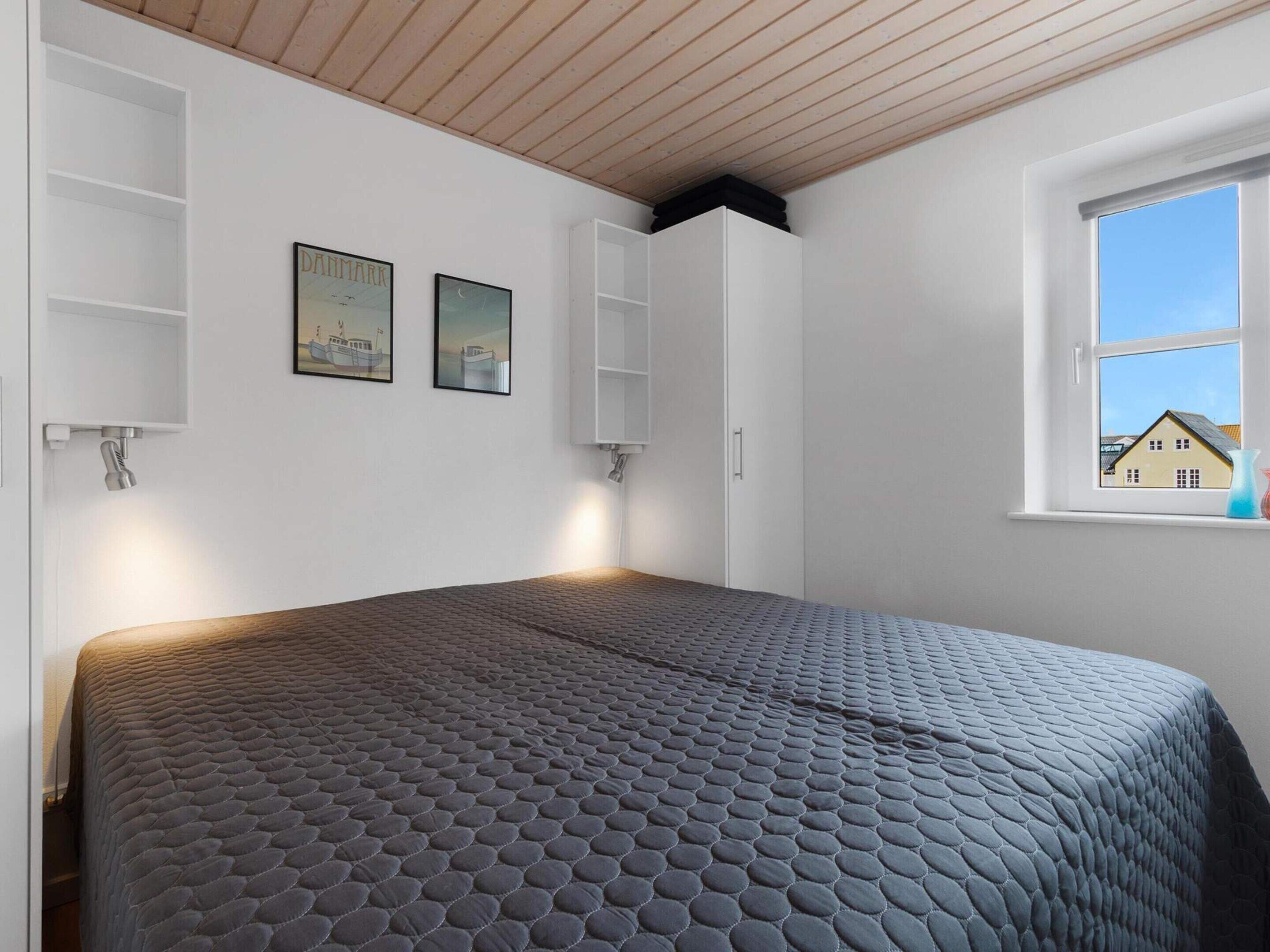 Une chambre avec un grand lit, des murs blancs et une fenêtre donnant sur une maison.