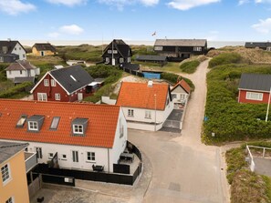 A coastal residential area with houses featuring red and white exteriors, some with thatched roofs, and a sandy beach in the background.