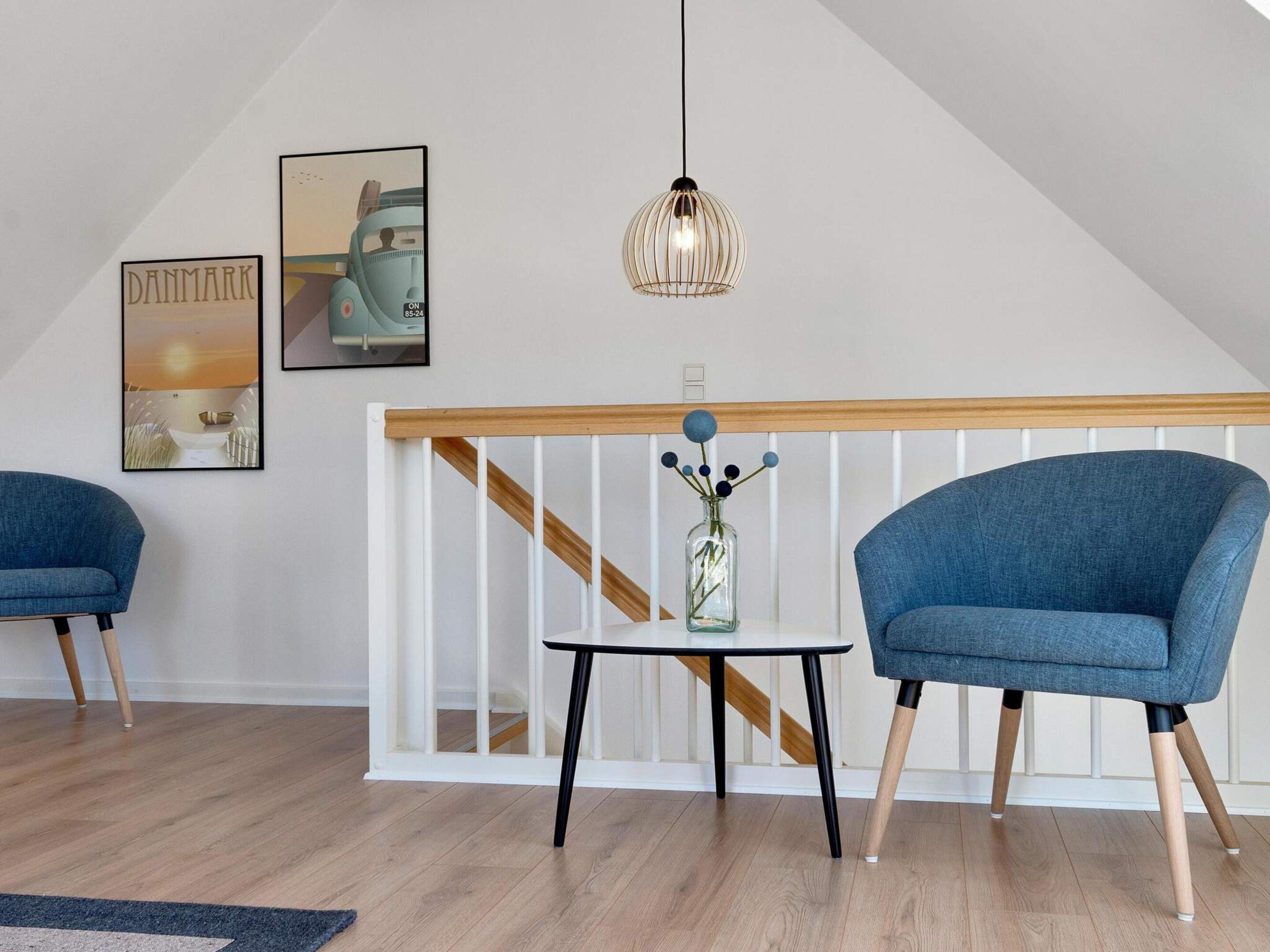 Un interior moderno con dos sillones azules, una mesita con un florero y una lámpara colgante.