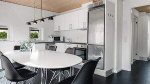 A modern kitchen with white cabinets, a stainless steel refrigerator, and a dining area with a white table and black chairs. - 5 Star Holiday Home in Lokken (Lokken)