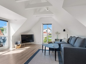 Una sala de estar moderna con un televisor de pantalla plana, un sofá, una mesa de centro y un ventanal con vistas al exterior.