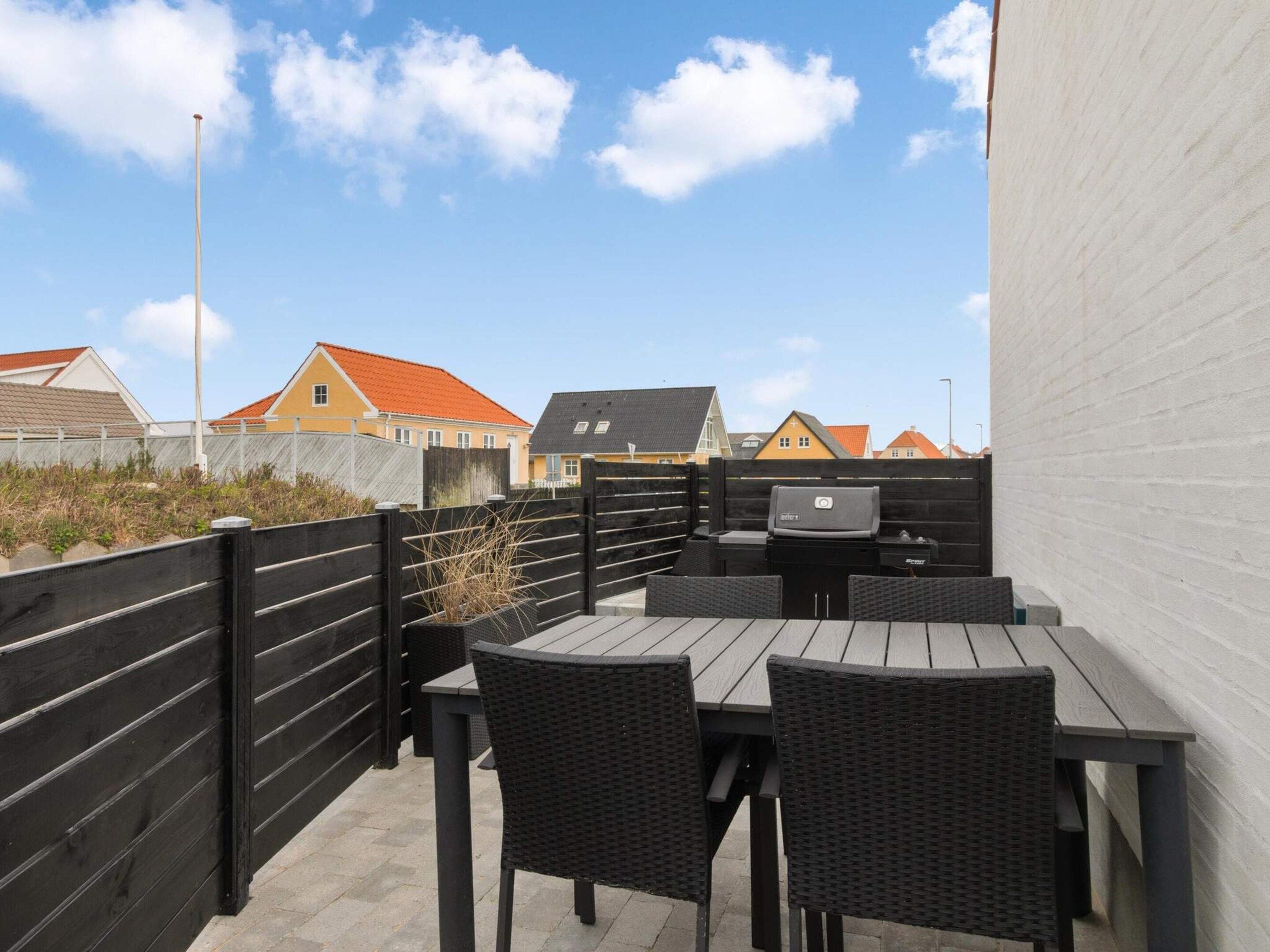 An outdoor patio with a table and chairs, a grill, and a view of houses in the background.