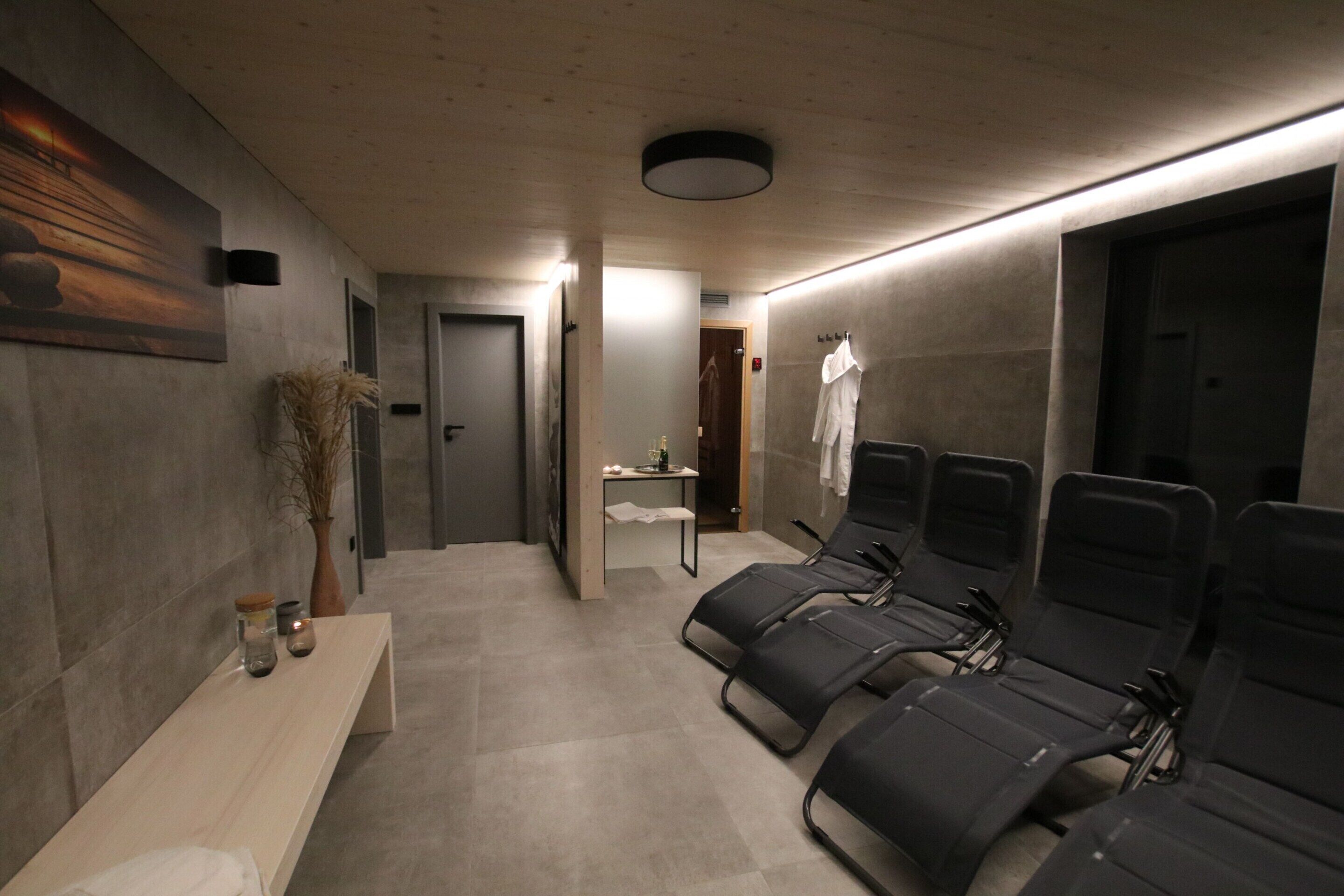 A modern spa room with a long bench, a small table with candles, and several massage chairs.