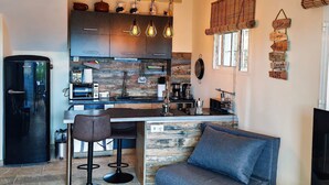 A modern kitchen with a central island, bar stools, and a grey sofa in a living area. - Casa Palmu apartment - A peaceful and relaxing oasis in Golf del Sur, Tenerife (Golf del Sur)