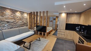 Ein modernes Wohnzimmer mit Steinwand, Holzvertäfelung, einer Couch, einem Fernseher und einer Küchenzeile mit schwarzem Arbeitsplatz und Geräten.