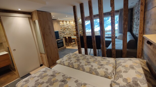 Ein Schlafzimmer mit Bett, Holzbalken, einer Steinwand, einem Essbereich und Blick auf Berge.