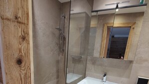 Ein modernes Badezimmer mit einer gläsernen Duschkabine, einem hölzernen Waschtisch und einem Spiegel über dem Waschbecken.