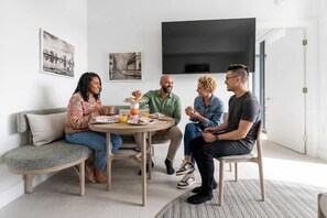 A group of four people seated around a round table in a modern living room with a sofa and a flat-screen TV mounted on the wall. - RumRunner, Downtown, Pool, Gym, Full Service Tower (Miami)