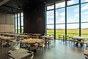 Een ruime eetruimte met meerdere tafels en stoelen, grote ramen met uitzicht op het landschap.